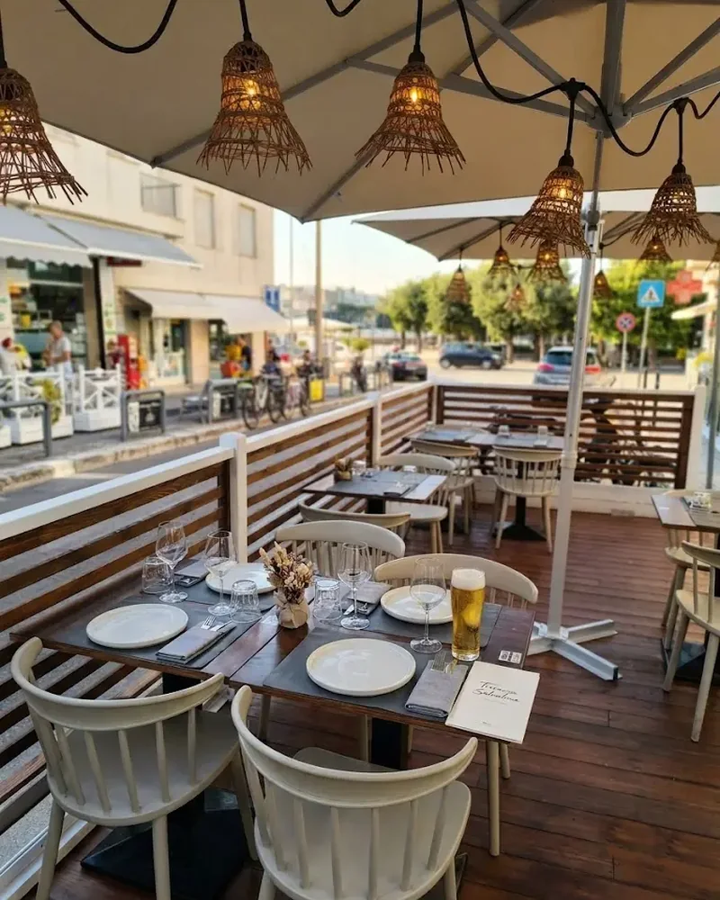 Dehors di Chill Out a Otranto: tavoli apparecchiati sotto gli ombrelloni con lampade in rattan su pedana in legno